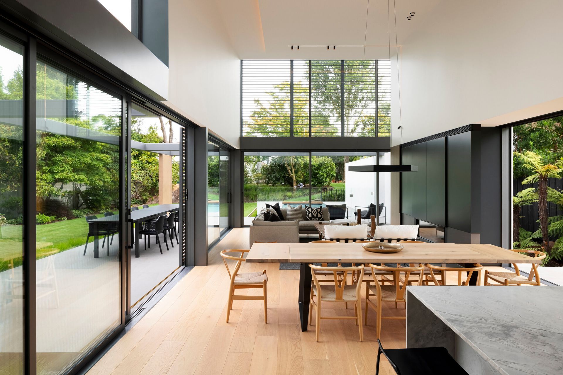The first living area is an expansive, double-height space. The sightline naturally flows through the large sliding doors towards 180-degree views of the established garden and pool.