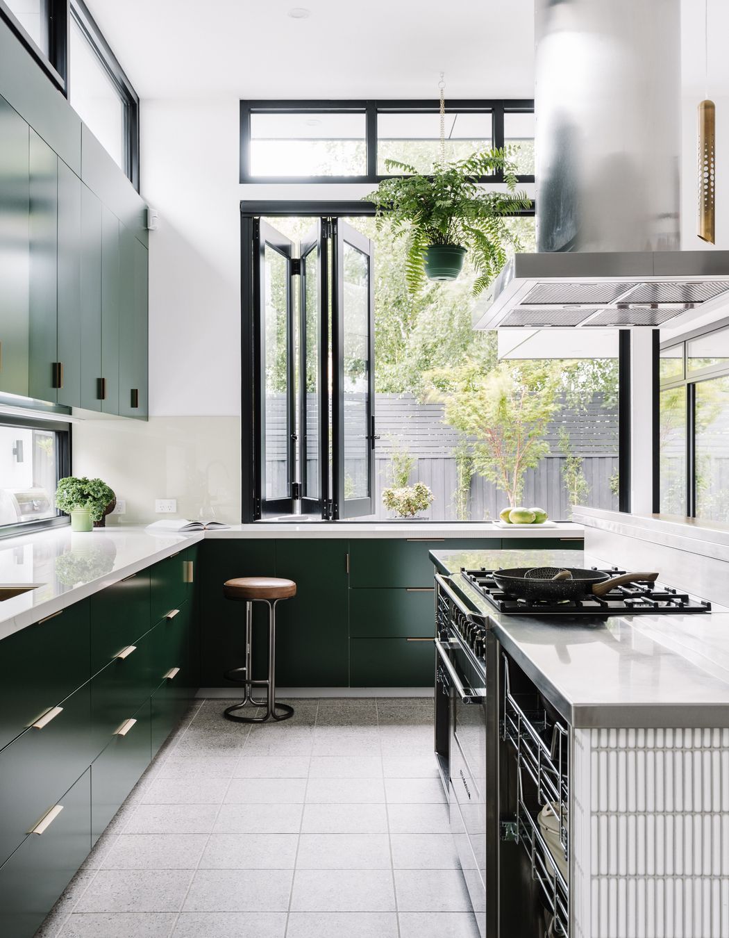 The kitchen island workspace is stainless steel with custom steel rack draws providing easy access to pots and pans. The rest of the joinery is 2pac dark green with a Dekton glacier benchtop.