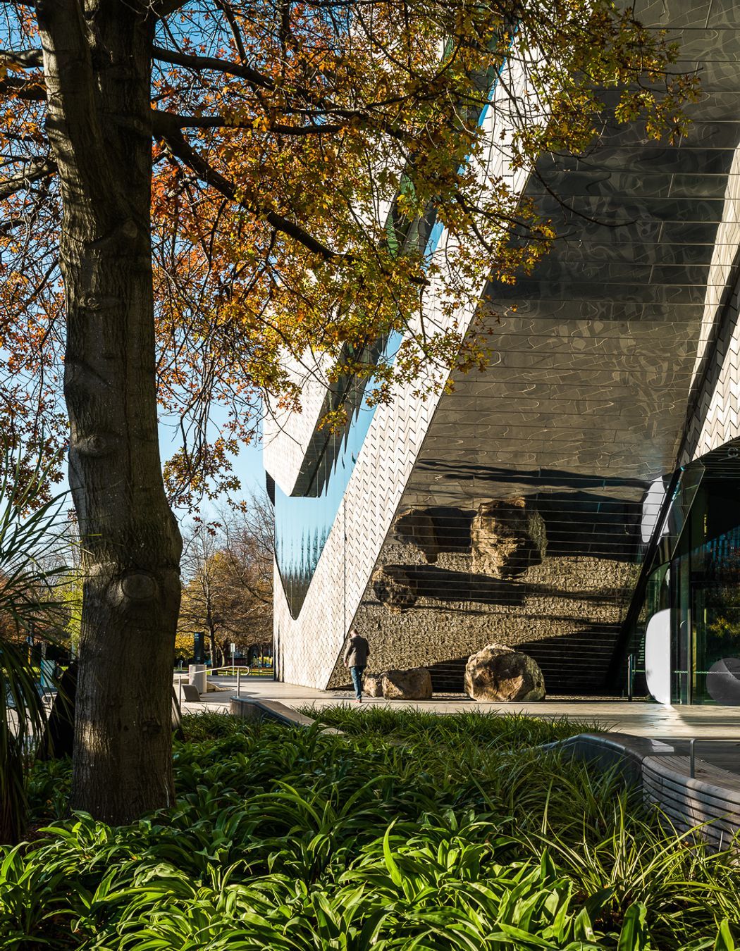 The mirrored façade reflects the patterned pavers at the building's entrance.