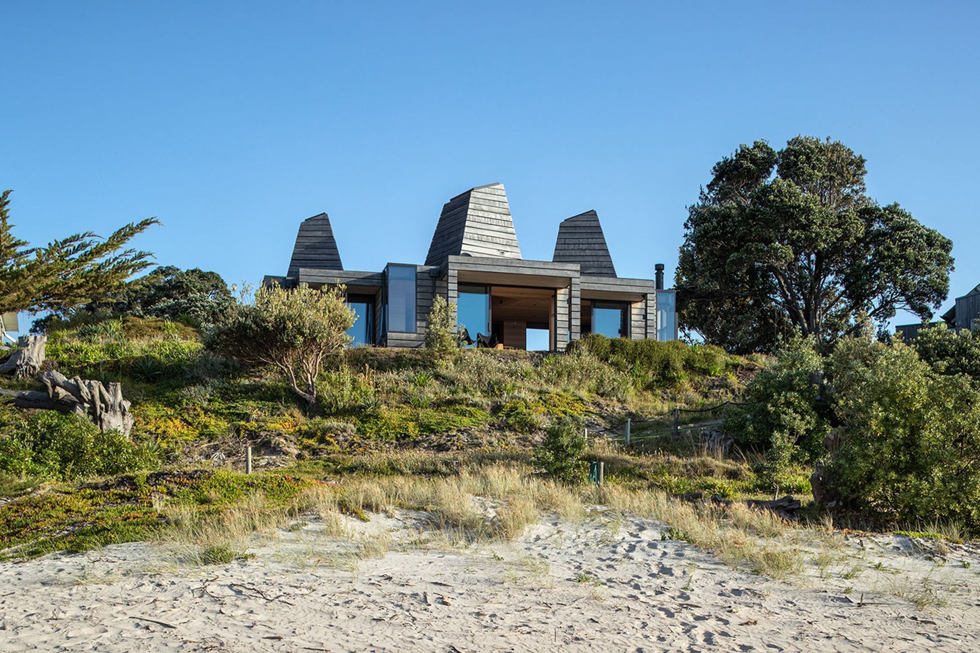 The site rests on the crest of a sand dune, overlooking the ocean and the shadowed curves of distant hills.