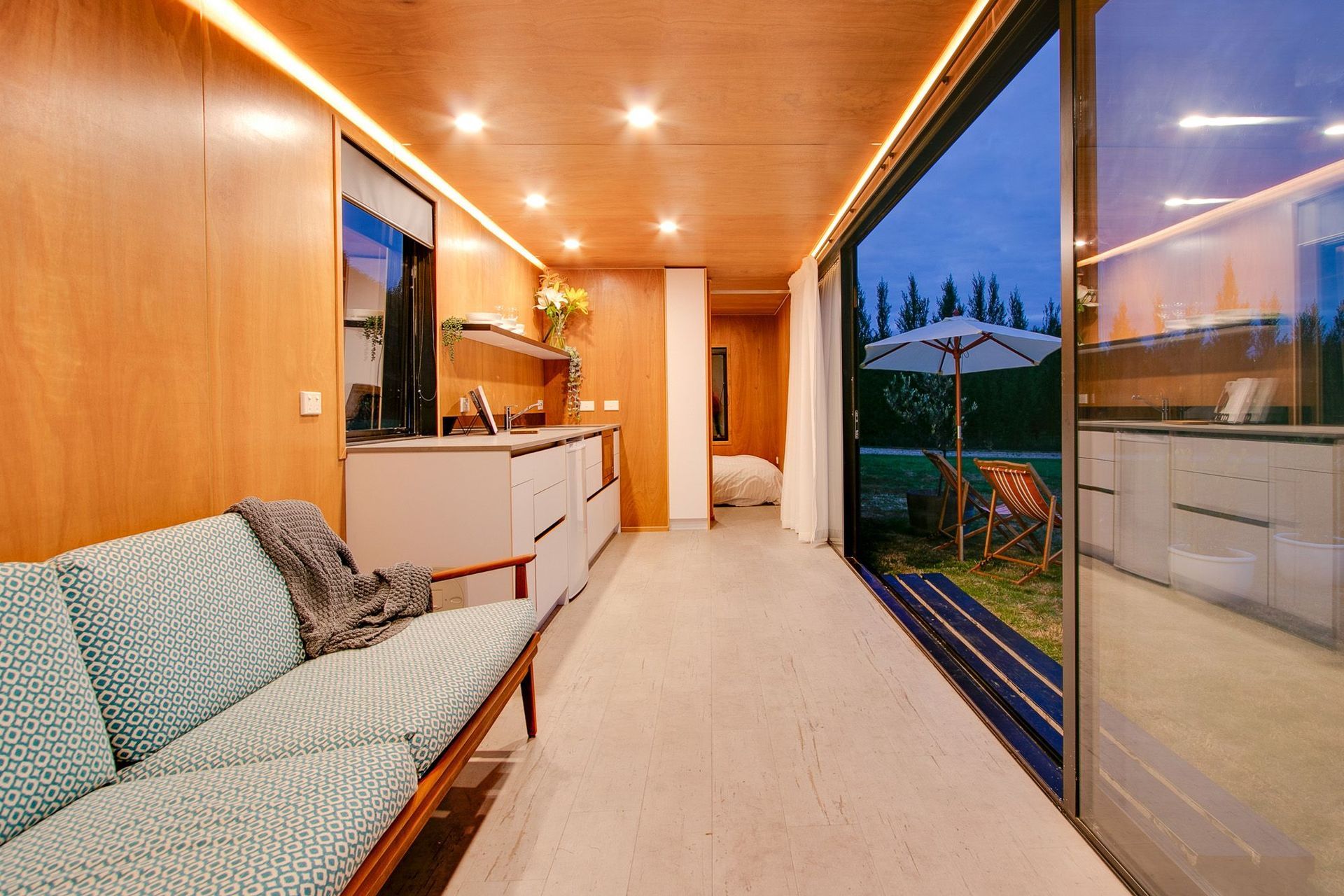 An interior clad with red plywood and strong recessed and strip lighting add great warmth to this shipping container home