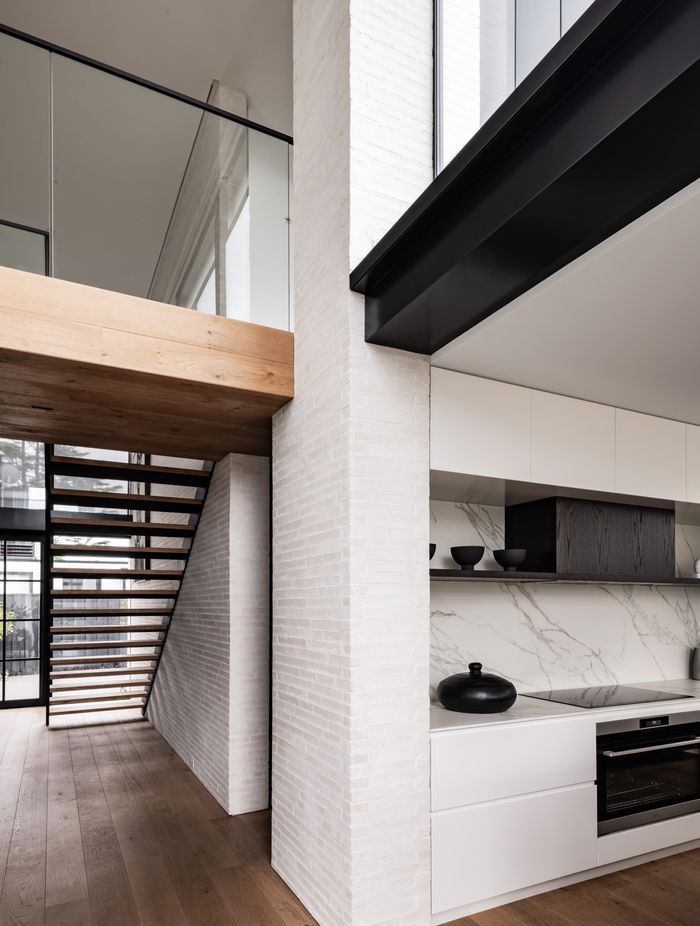 The bridge at the top of the stairs leads to two bedroom suites, and a powder room is tucked underneath. Glazing over the kitchen brings light into the double height living room.