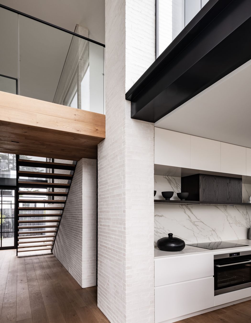 The bridge at the top of the stairs leads to two bedroom suites, and a powder room is tucked underneath. Glazing over the kitchen brings light into the double height living room.
