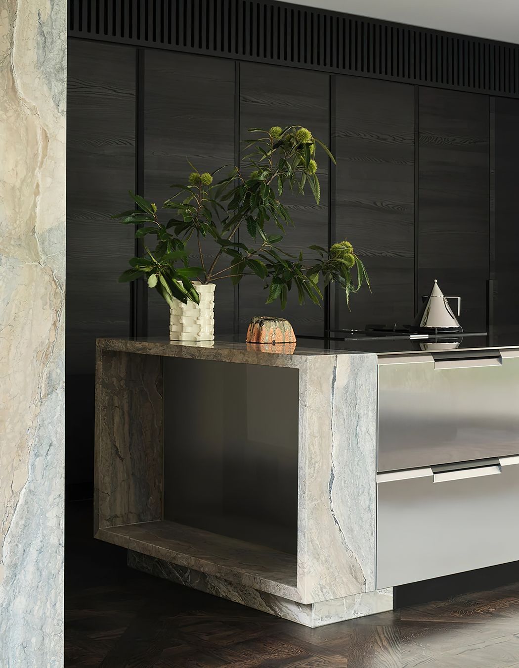 The stainless steel Shape kitchen by Poliform features a tapered cut and sleek integrated handles, perfectly complementing the marble columns that anchor the kitchen island.