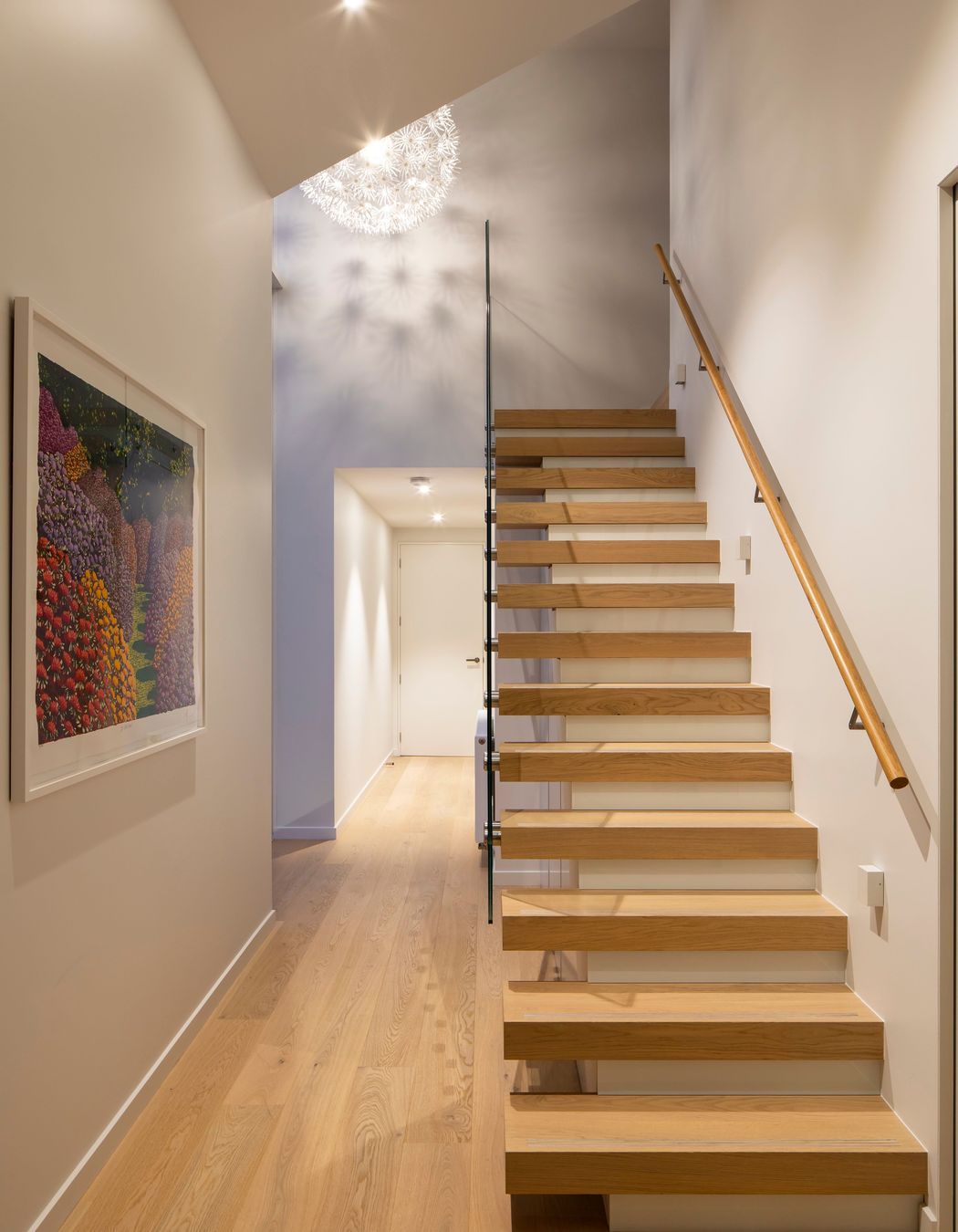 A floating staircase leads to the upper-storey master bedroom suite, while the hallway leads to secondary bedrooms, a bathroom and garage.