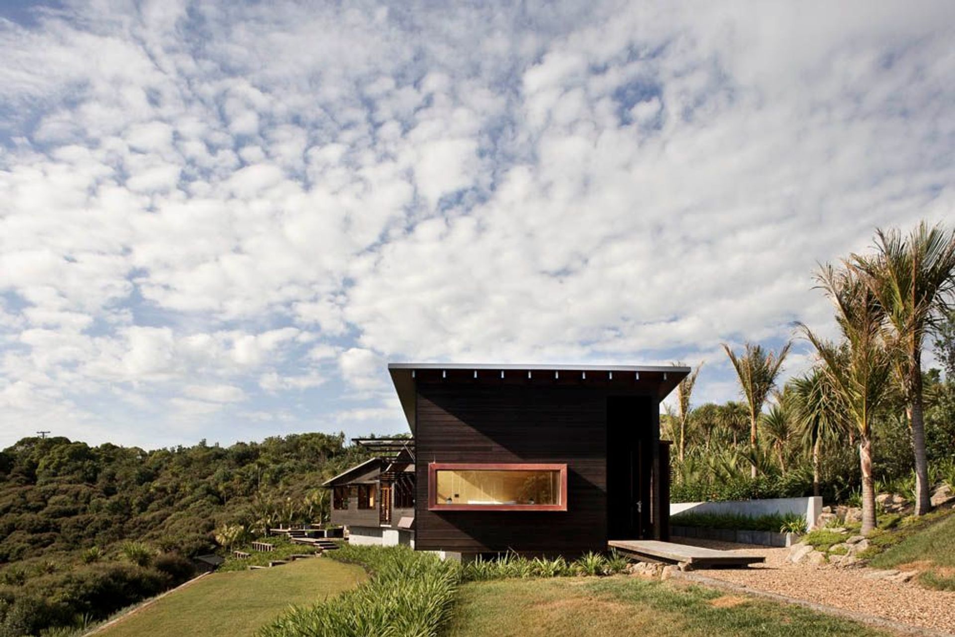 Owhanake Bay house utilises horizontal weatherboards in a dark stain, drawing it lower to the ground and making it recessive in its bush location. By Strachan Group Architects. Photo by Patrick Reynolds.