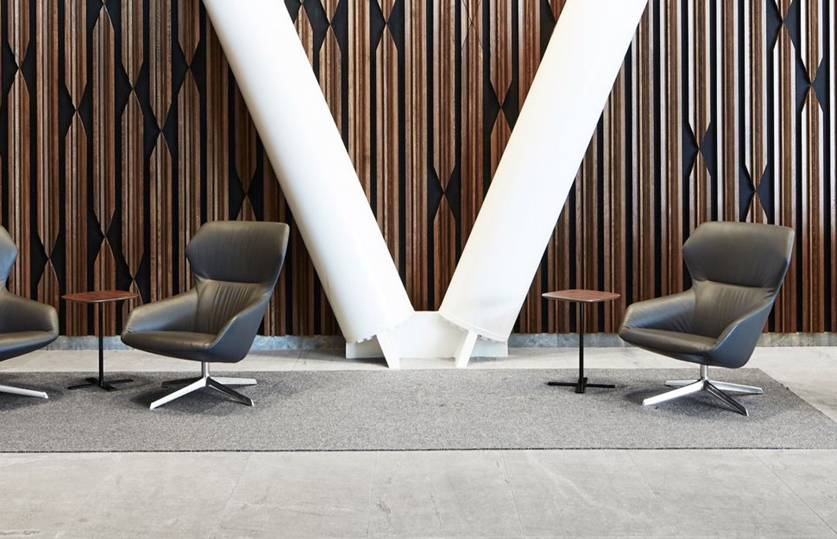 The lobby of XXCQ utilises natural materials, with a timber-panelled feature wall, angular reception desk in polished stone and brass, and curvaceous Scandinavian-style leather-clad chairs.