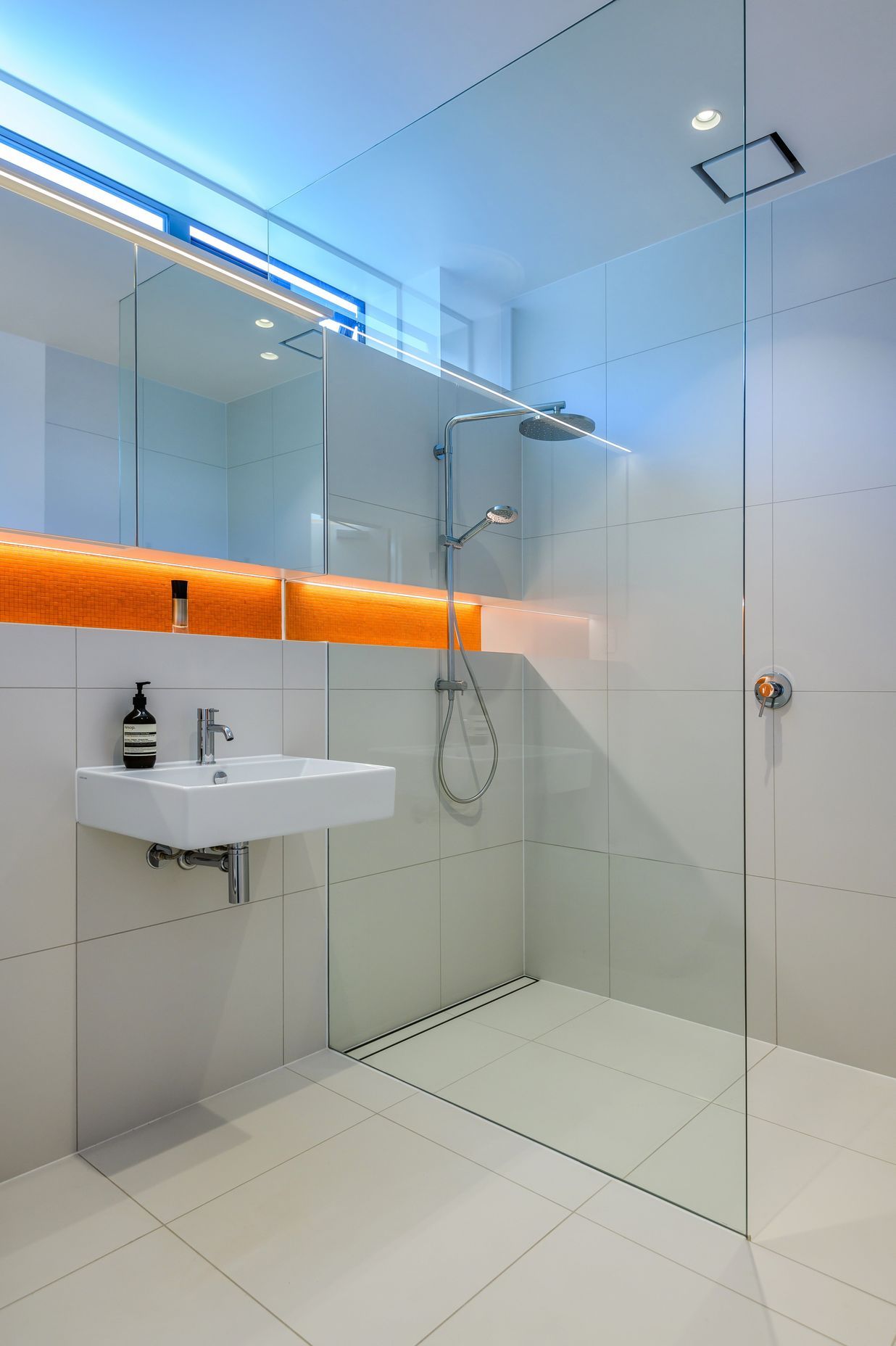 A pop of orange in the tiling and LED lighting elevate this otherwise all-white bathroom.