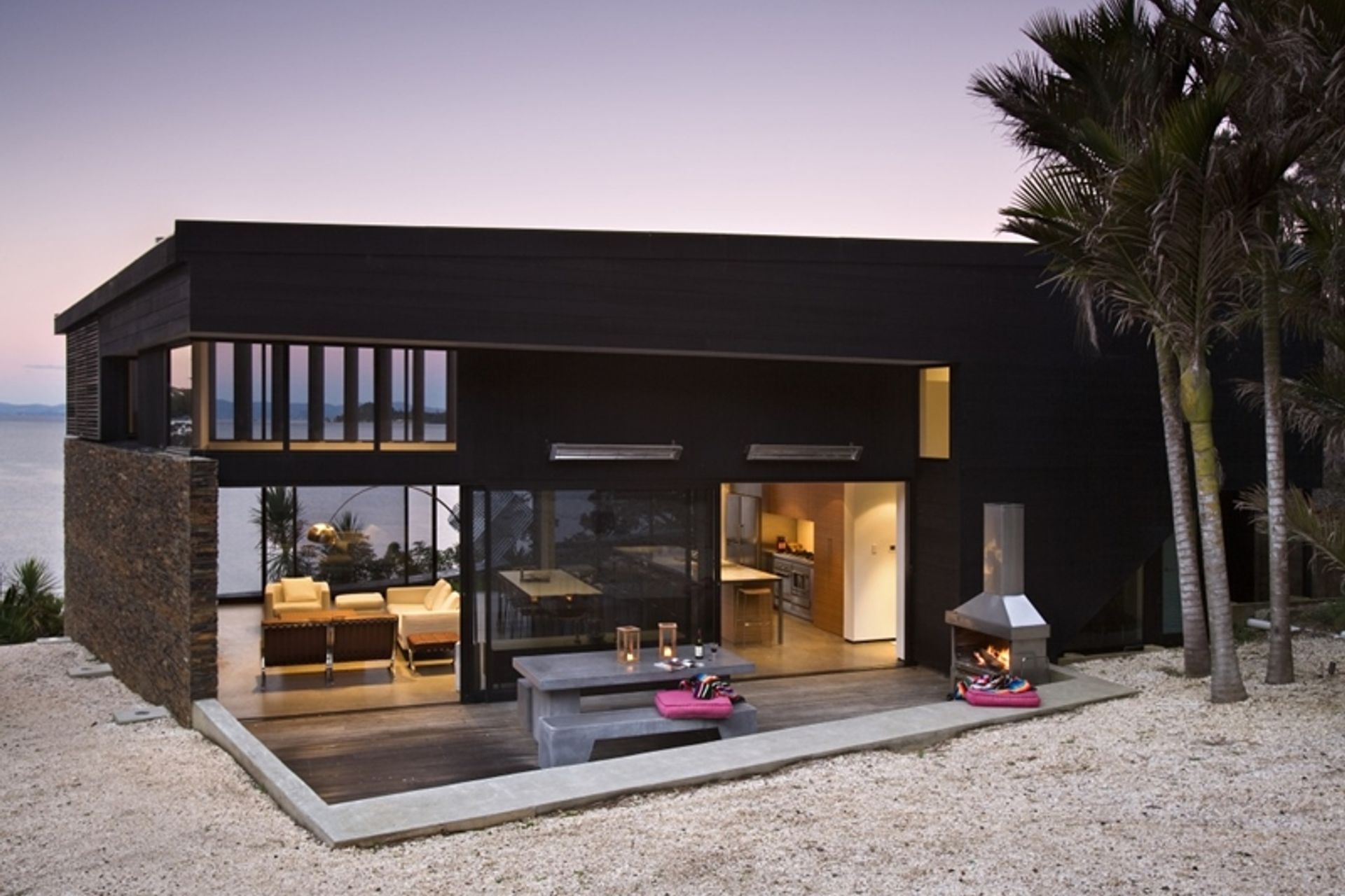 Bright outdoor cushions in the fuschia accent colour bring a holiday feel to this modern Waikopua beach house by Daniel Marshall Architects.