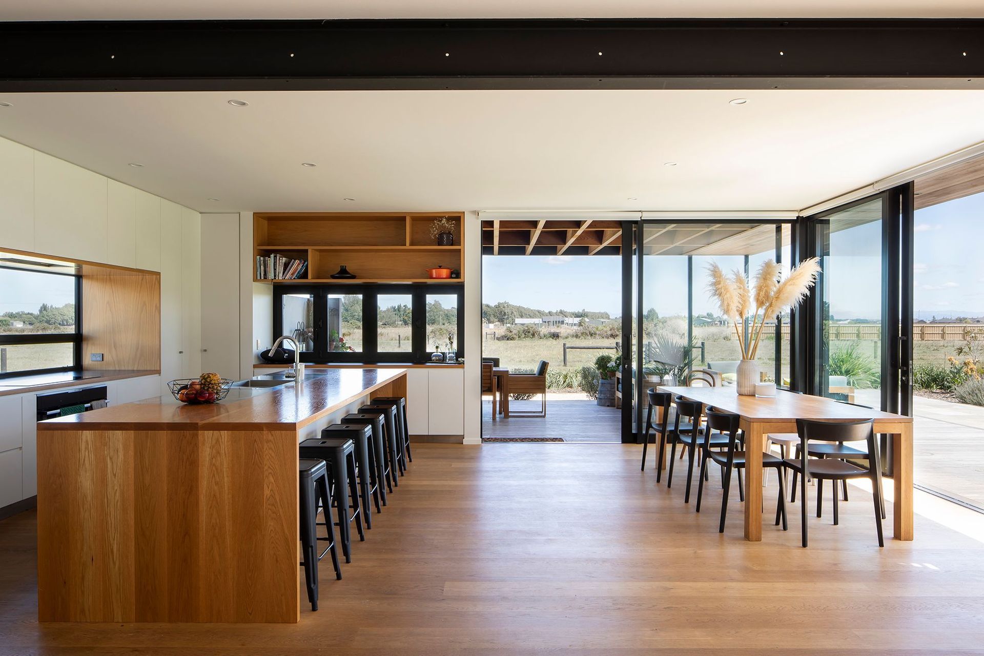 The open-plan kitchen and dining space looking through to the outdoor room and the rural landscape. From the kitchen, the homeowners can also observe visitors coming up the driveway.