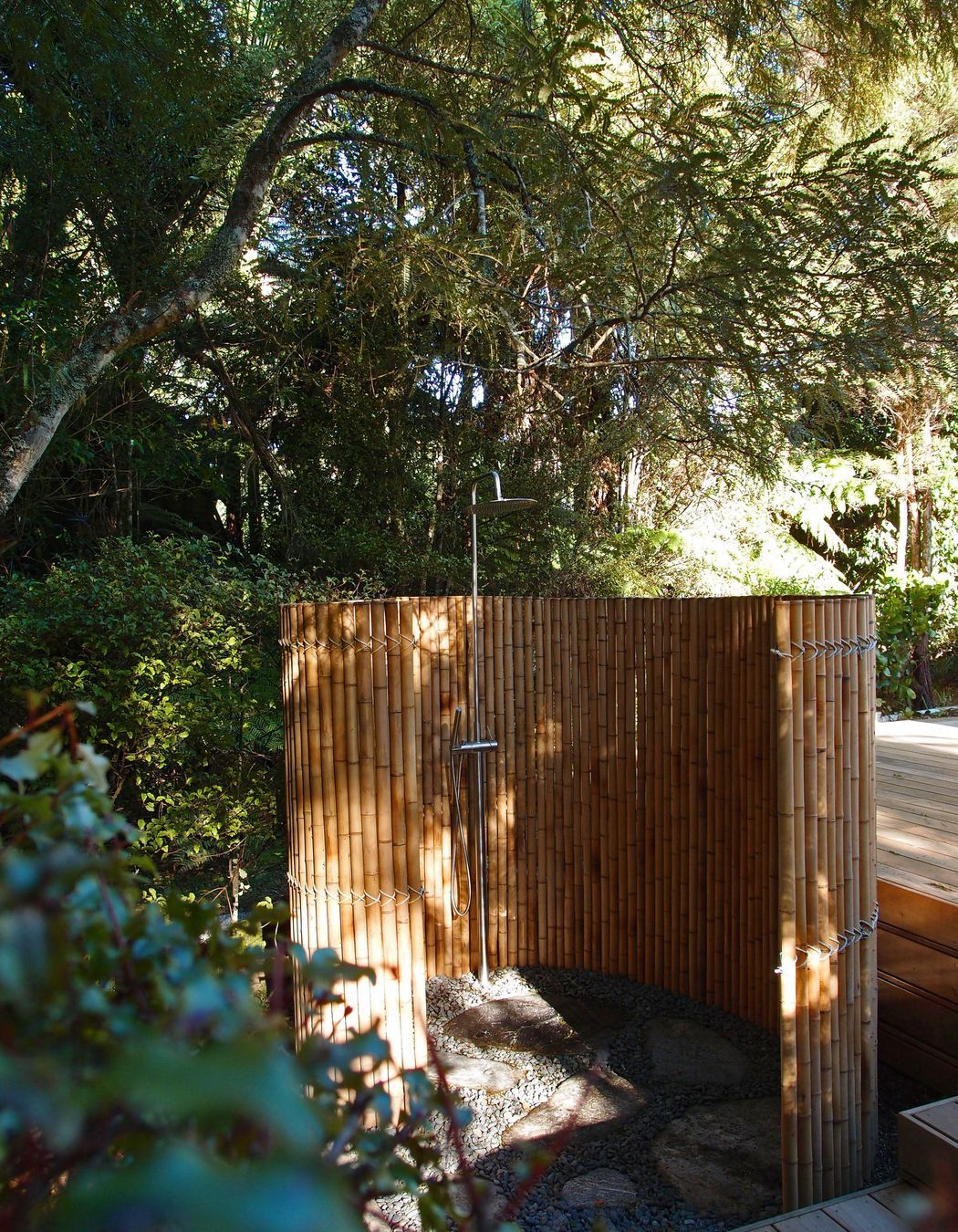The outdoor shower is enclosed by a bamboo screen in a spiral. The floor is smooth schist and rounded pebble.