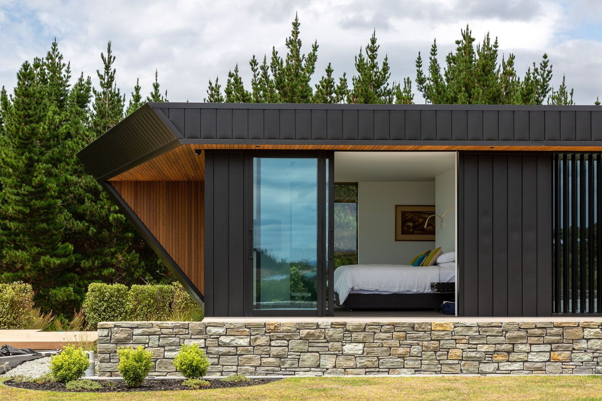 The cedar-clad overhangs create dramatic angles, a sense of movement and a visual focal point in their departure from the black vertical aluminium cladding that graces the rest of the exterior. 