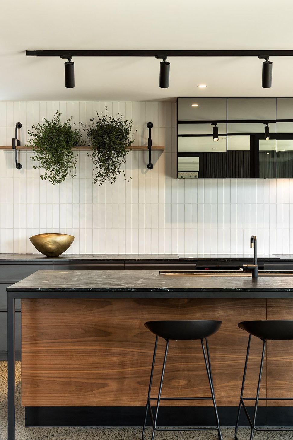 The kitchen combines bespoke walnut cabinetry with a black granite island and mirrored overhead cabinets, creating a rich and timeless material palette at the heart of the home.
