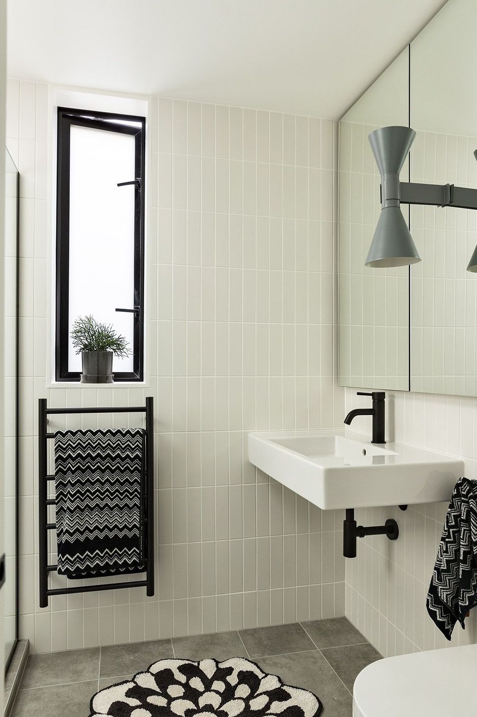 The ensuite combines textured tiles, black fittings, bespoke walnut cabinetry and a sculptural grey wall light to create a calm and elegant retreat.