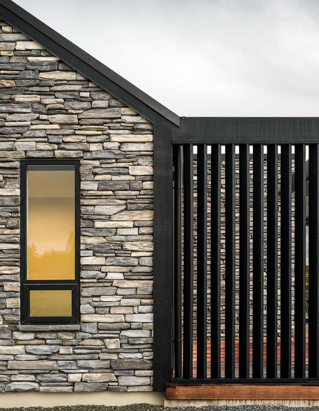 Dark stained vertical cedar frames the main body of the house with gable end accents and feature walls of Schist stone combining to create a solid and defined house.