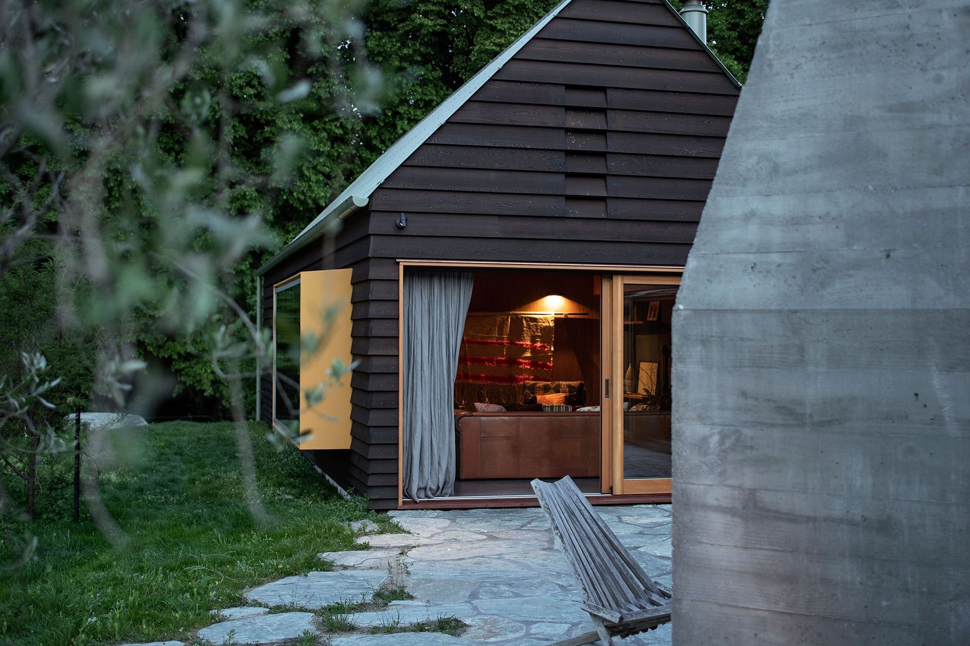 The living space has a yellow pop-out reading window that overlooks the lawn. The schist pavers have undefined edges that seem to dissolve into the lawn.