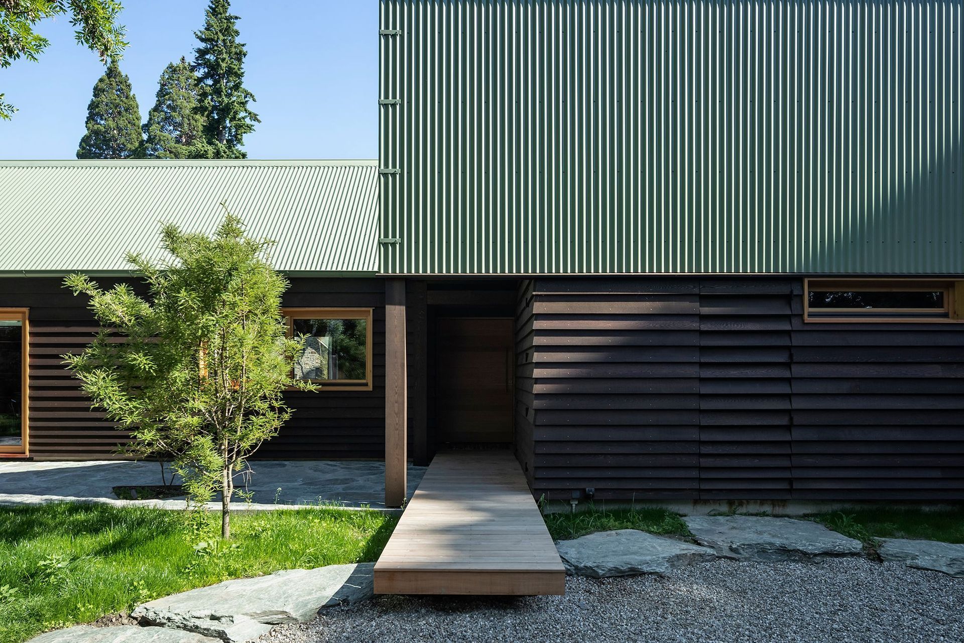 At the edge of the chisel form, an entry boardwalk floats over large stones before disappearing under the chiselled roof to form a semi-enclosed walkway.