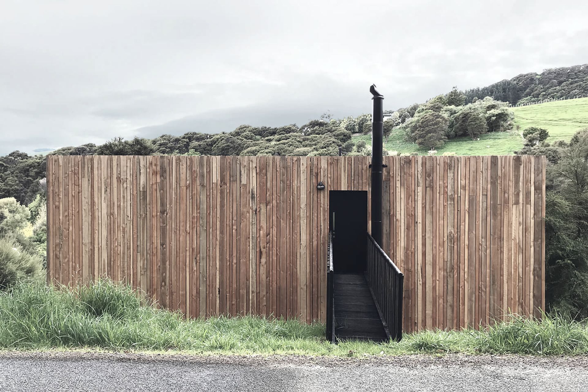 The black entrance forms a void within the timber-clad envelope which wraps around the home and sympathetically sits within the manuka-clad and rural landscape.
