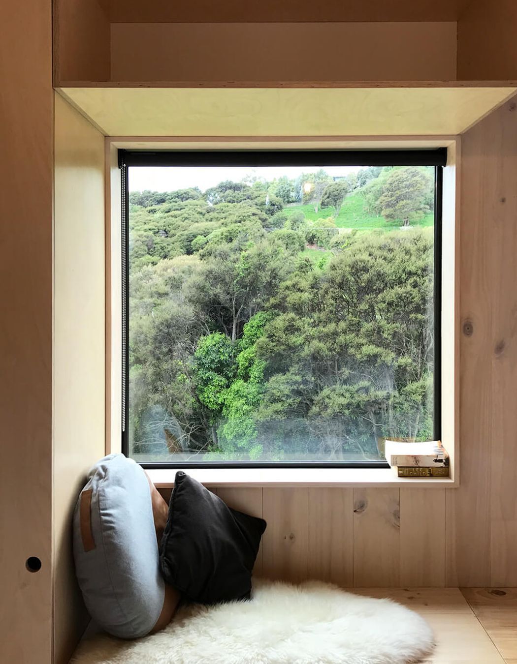 A built-in window seat looks out to a manuka bush-clad hillside and grazing farm animals.