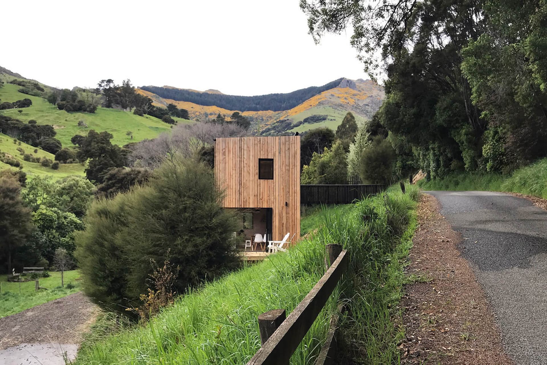 Akaroa Bach from the road showing the verticality of the home nestled into the steep slope with a bridged entranceway from the roadside.