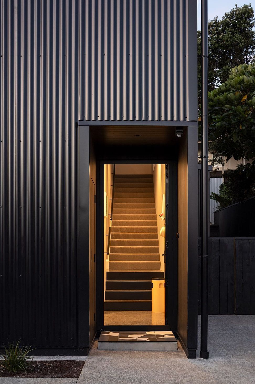 The welcoming front entrance frames a view directly through to the sculptural timber staircase beyond. Natural light draws visitors inside, offering an immediate glimpse of the home's carefully crafted interior