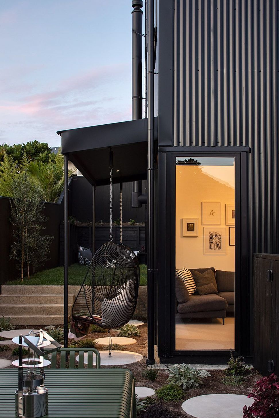 A closer view of the open-plan living area highlights the relationship between the dining space, kitchen and cosy snug. The black granite island, HAY pendants and L-shaped sofa create a layered family living environment that is both functional and inviting.
