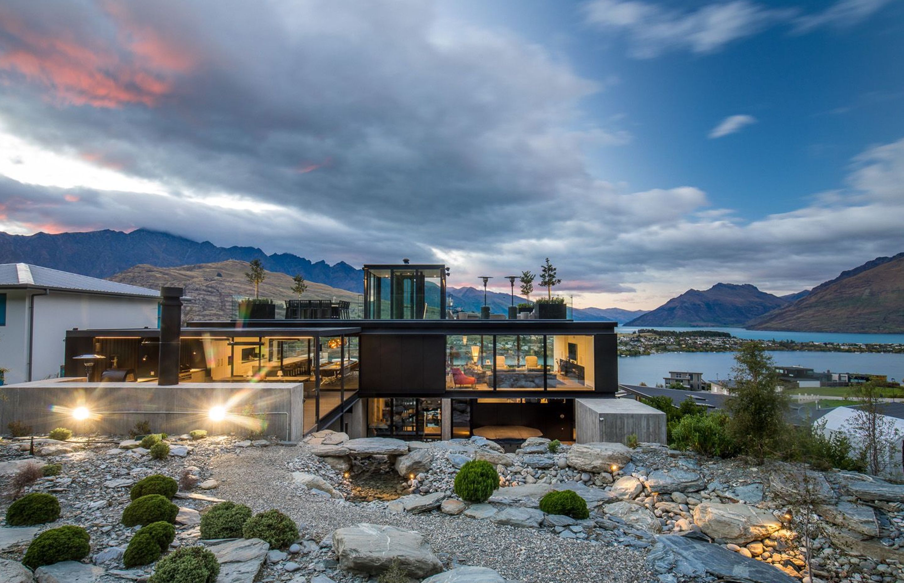 The north-facing elevation of Cascata House seen in context to Lake Wakatipu and the surrounding mountains, viewed from the rockery garden and stream.