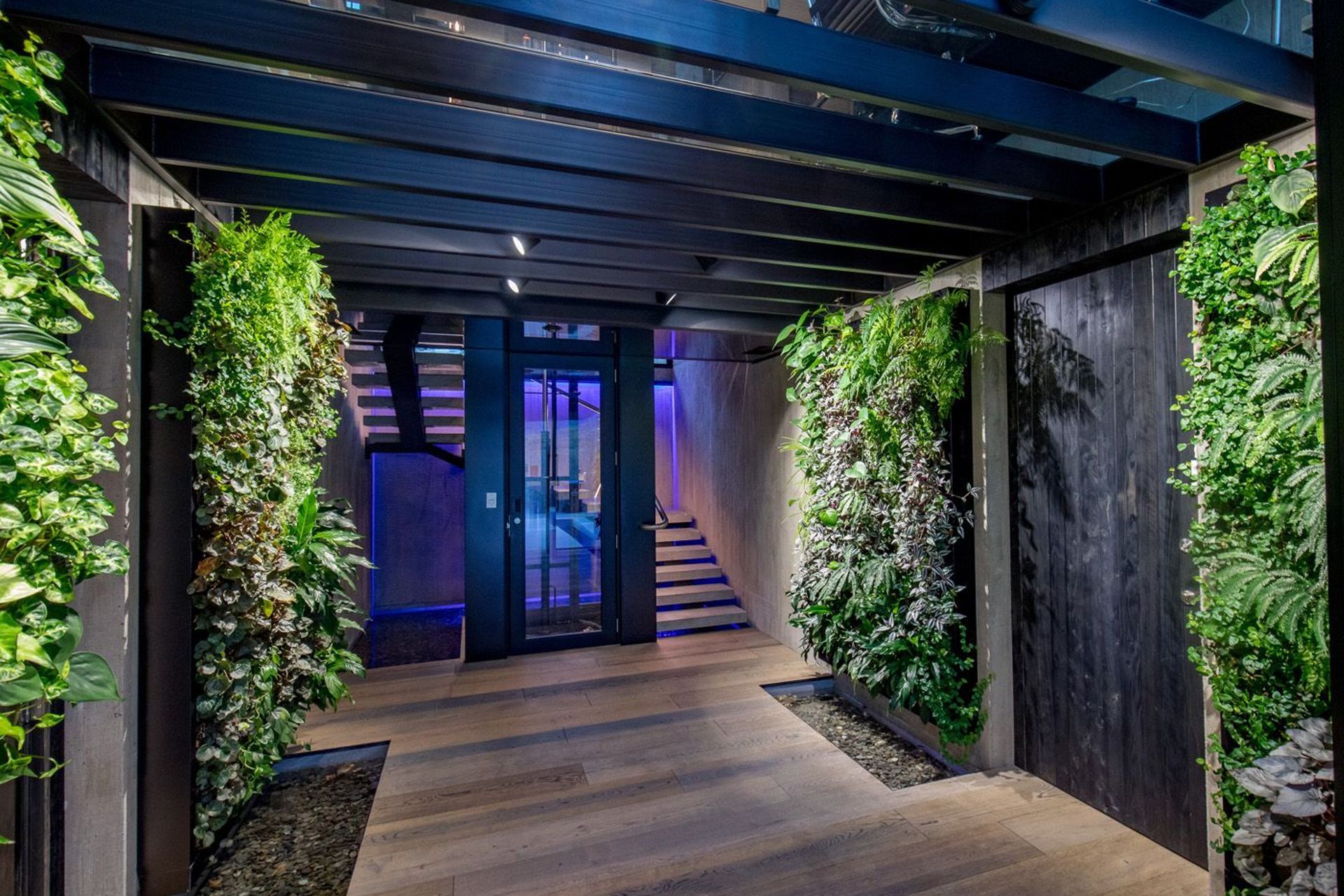 The entrance foyer, lined in vertical green walls, leading to the central lift shaft and stairwell, with a glass ceiling above, and an internal waterfall on the rear stairwell wall beyond.