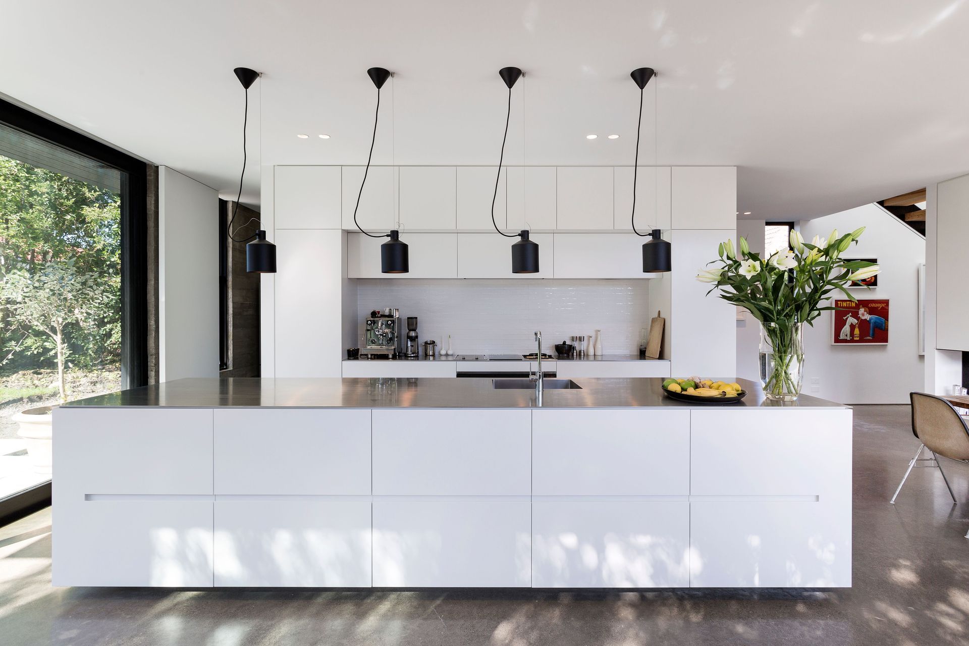 The monochromatic interior colour scheme includes an all-white kitchen with stainless steel benchtops and black lights and fixtures. 