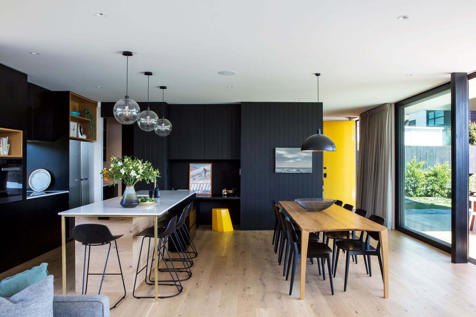In the kitchen, splashes of yellow in the door and a stool provide colourful accents to the neutral colour scheme of black. white and honey-coloured timber.