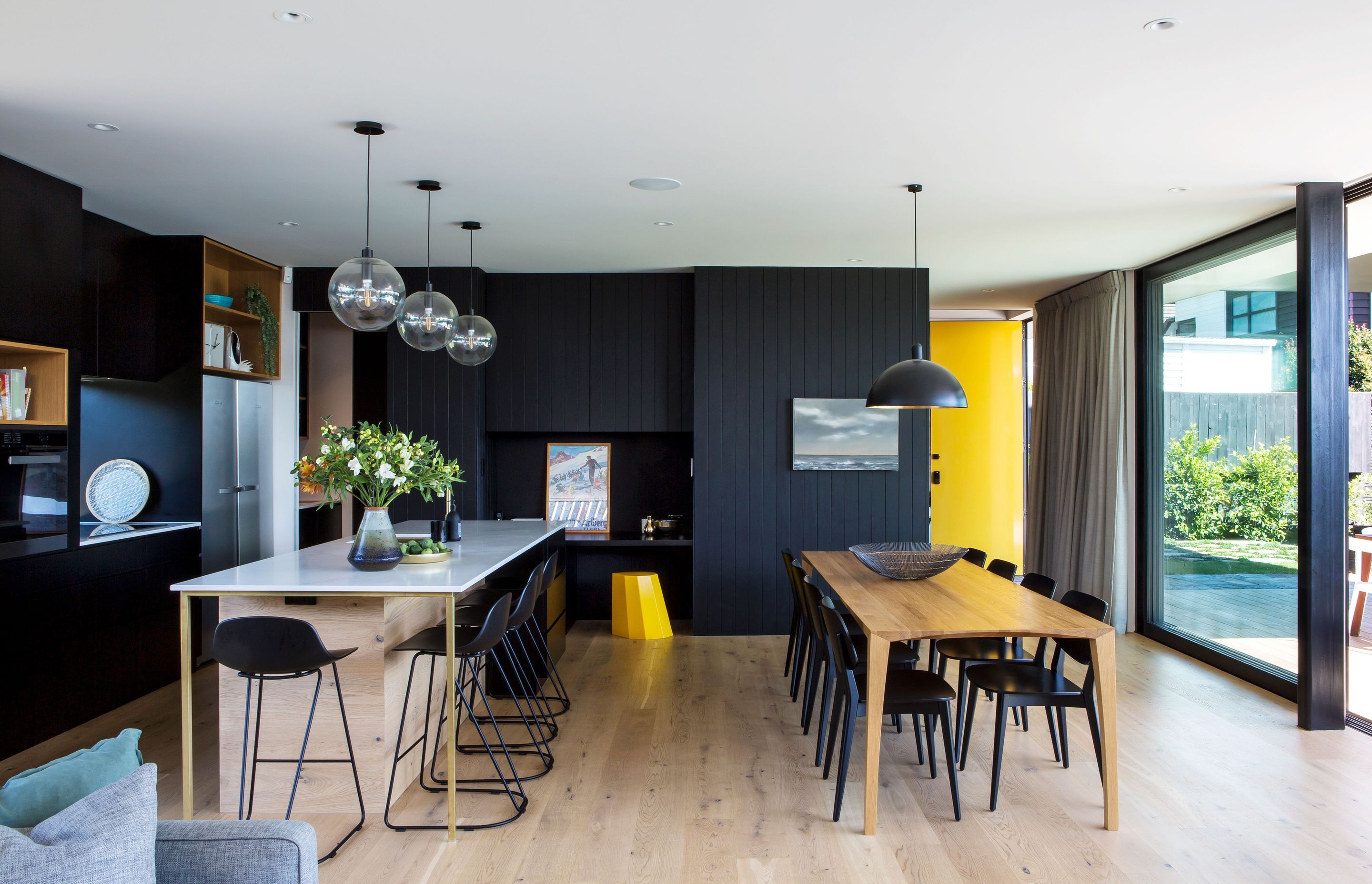 In the kitchen, splashes of yellow in the door and a stool provide colourful accents to the neutral colour scheme of black. white and honey-coloured timber.