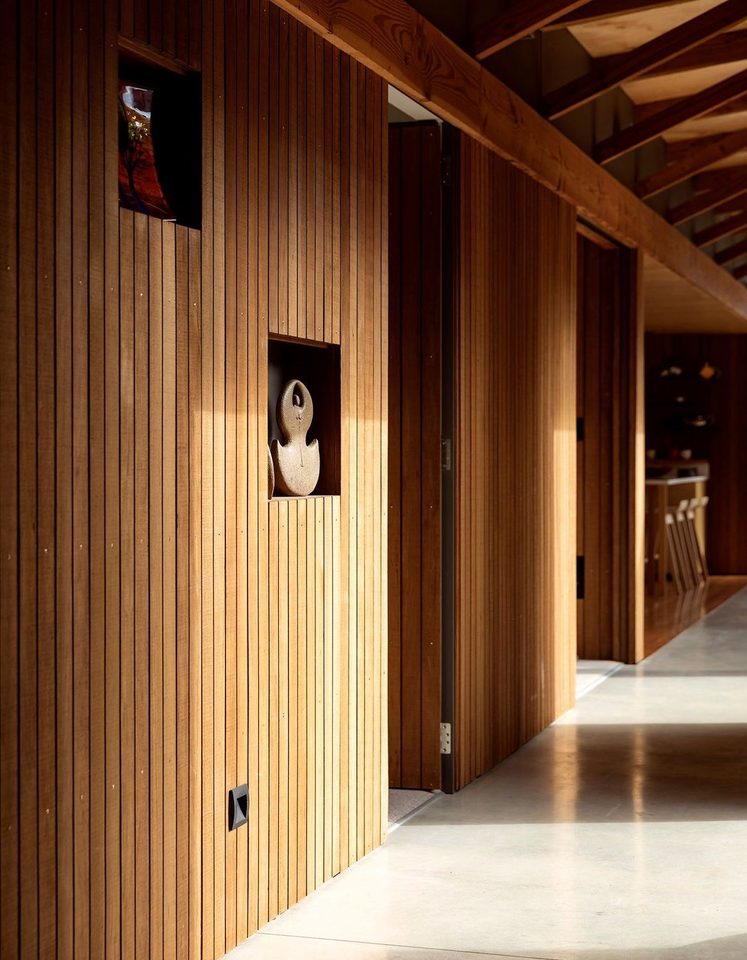 Beginning in the kitchen and winding through the entire central corridor, including the doors that lead into the bedrooms off it, the walls are clad in vertical shiplap totara that reaches up to meet the exposed timber ceiling.