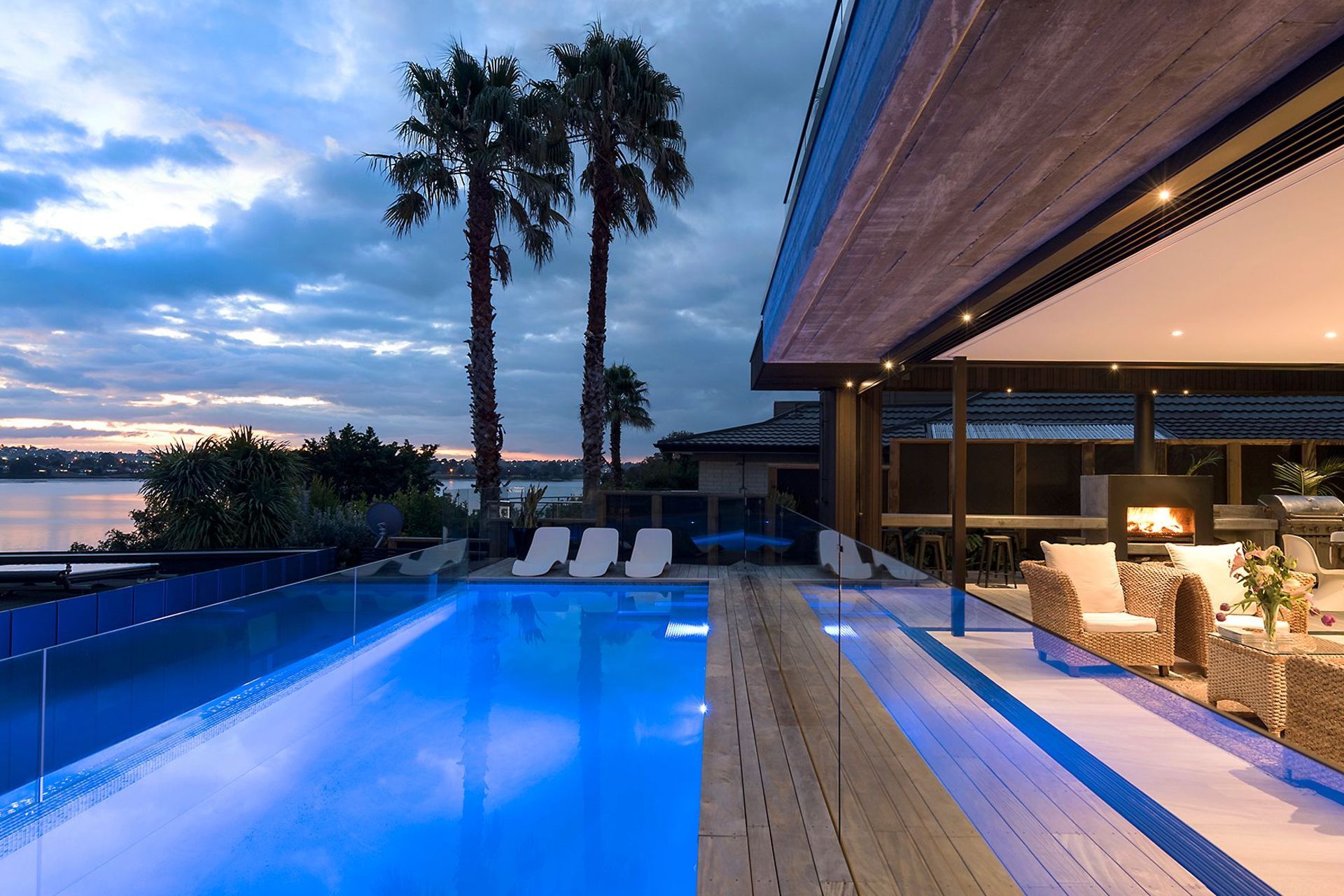 A night view of the blue-lit swimming pool gains a tropical feel from the shadows cast by mature palm trees and the setting sun.