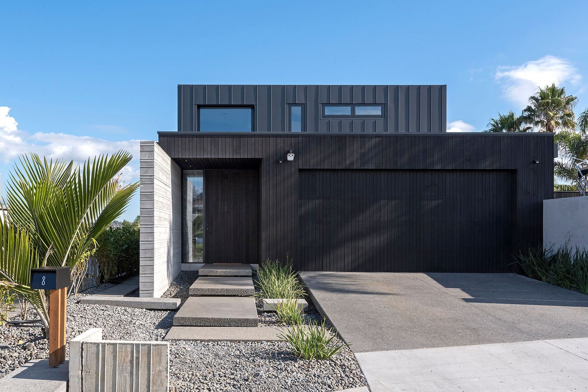The streetview of Island Life in the Suburbs showing its distinctive dark-stained cedar and seamed metal claddings, complemented by a shuttered insitu concrete feature wall at the main entrance.