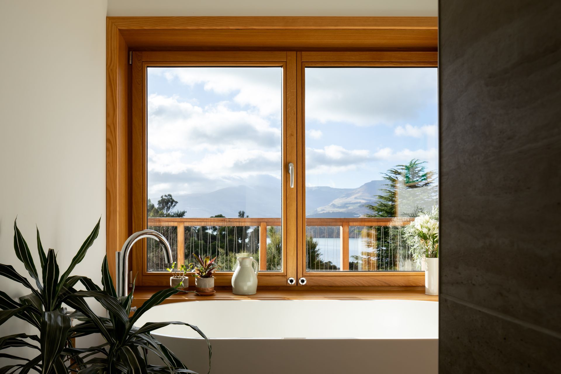 The timber window frames pop out of the house to create deep sills above a bathtub, highlighting the sensational view over Governors Bay.