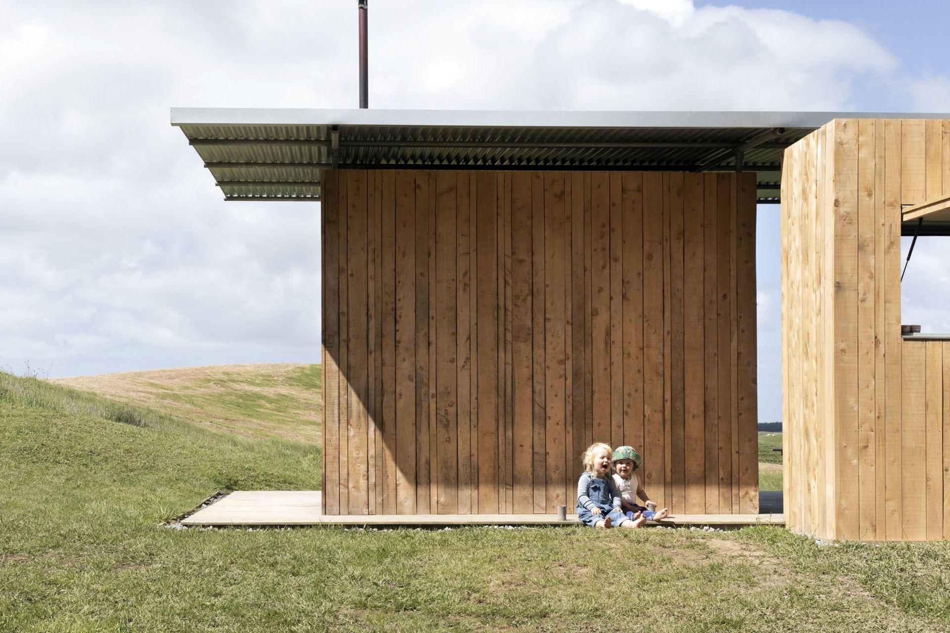 Two insulated macrocarpa-clad boxes sit beneath a classic Kiwi corrugated iron roof, creating a semi-sheltered space in between that encourages outdoor living.
