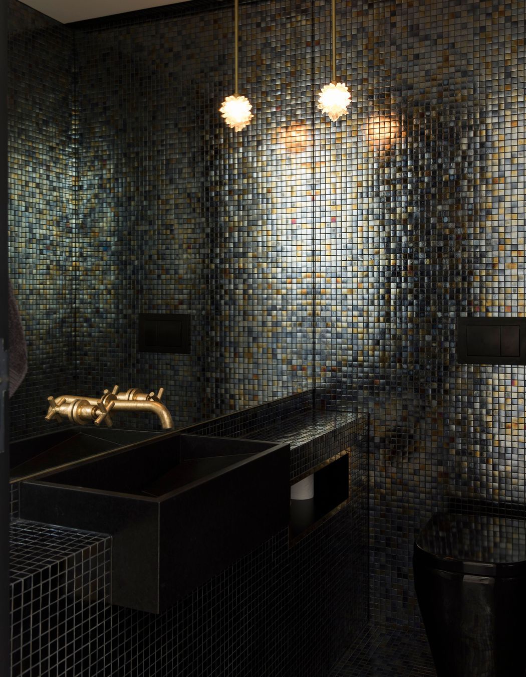This dark and moody bathroom .features brass taps and black cabinetry.