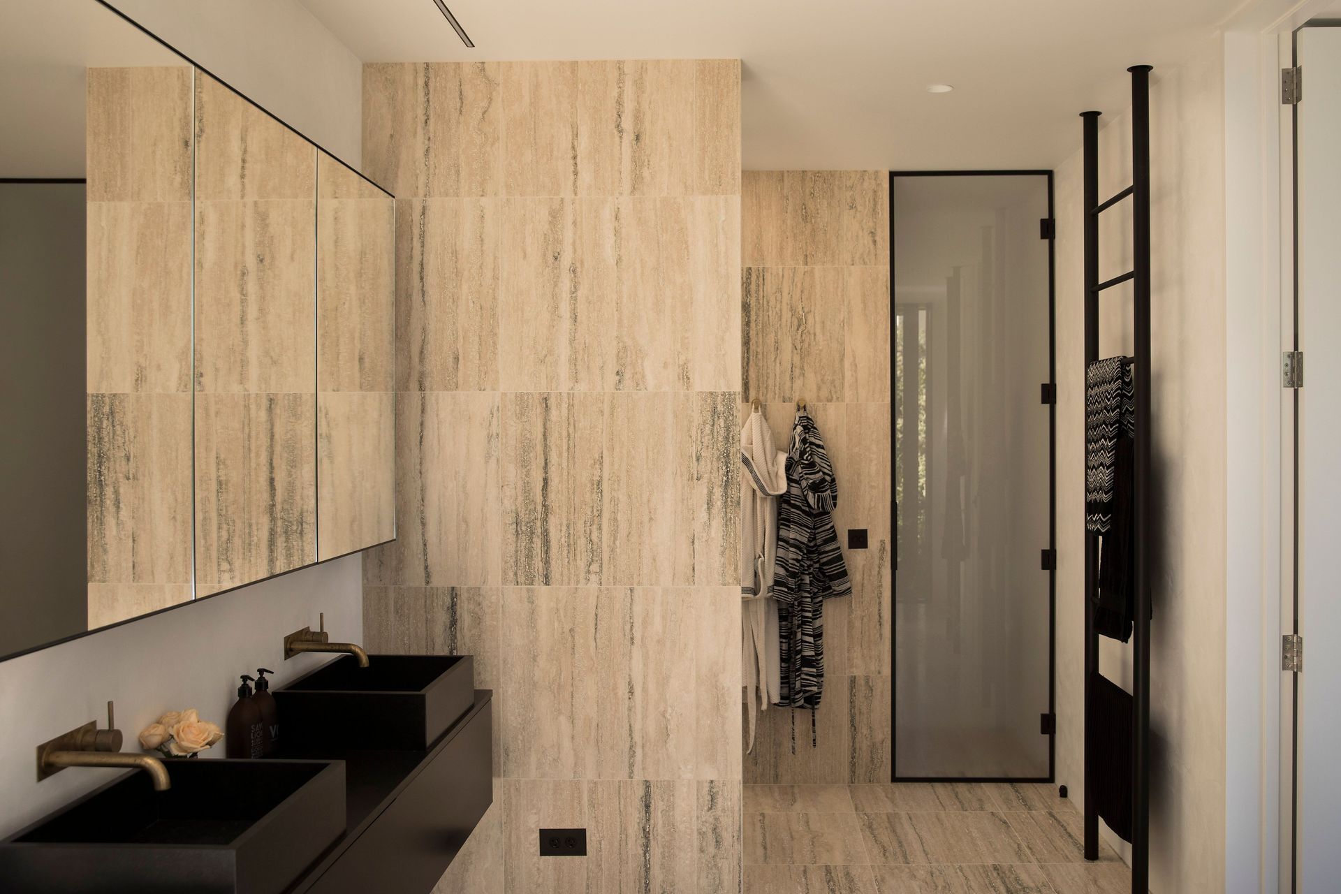 Light-coloured travertine stone tiles continue from the flooring onto the walls and cabinetry, creating a seamless high-quality finish.