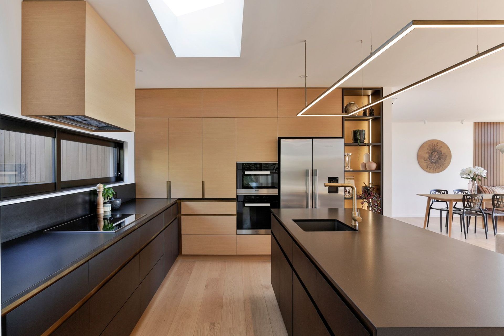 American oak veneer and brass accents add softness to the black lacquered cabinetry and granite benchtop, creating a balanced colour scheme.
