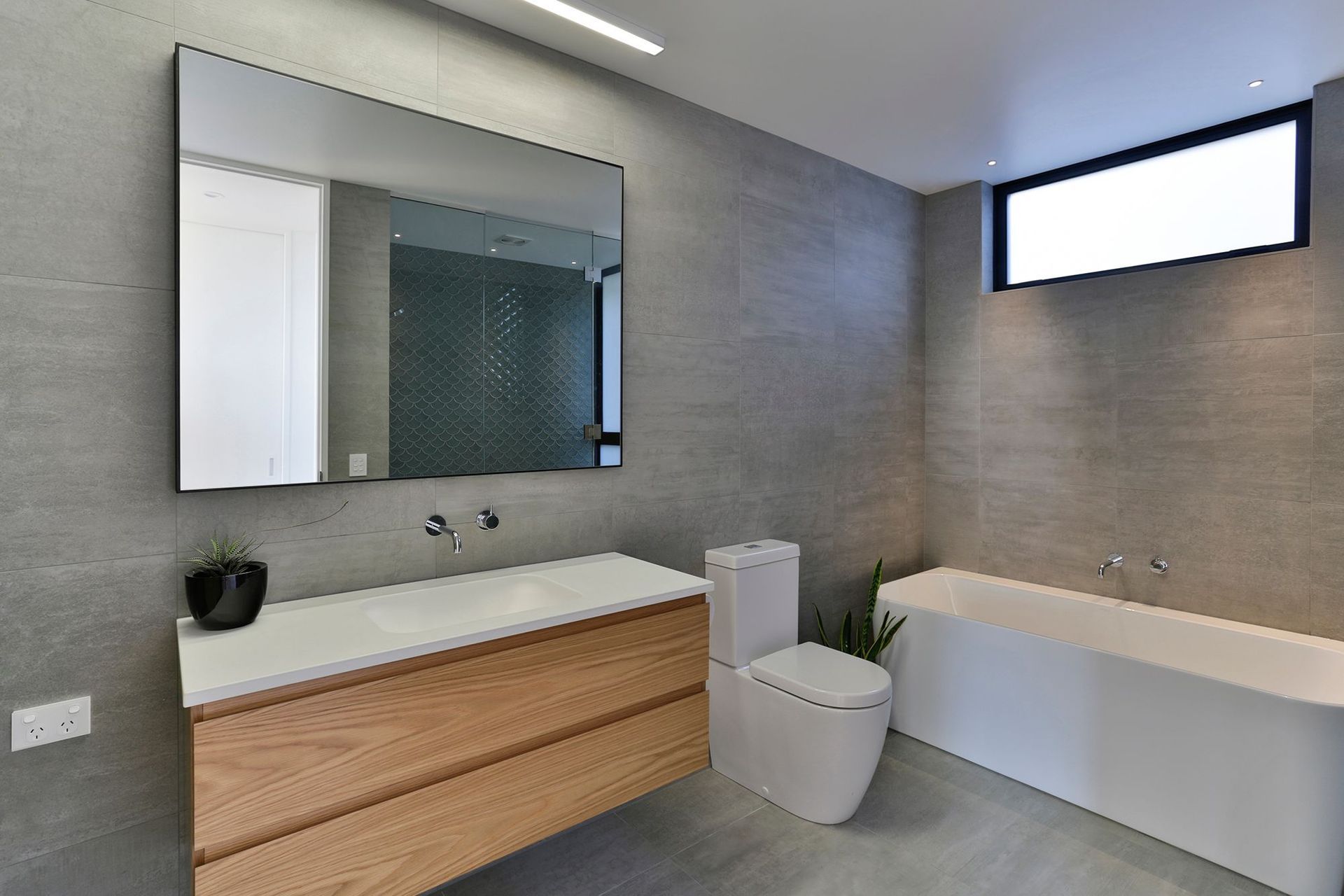 The bathroom continues the material palette of the house but is more subdued with the addition of stone tiling on the walls and floor.
