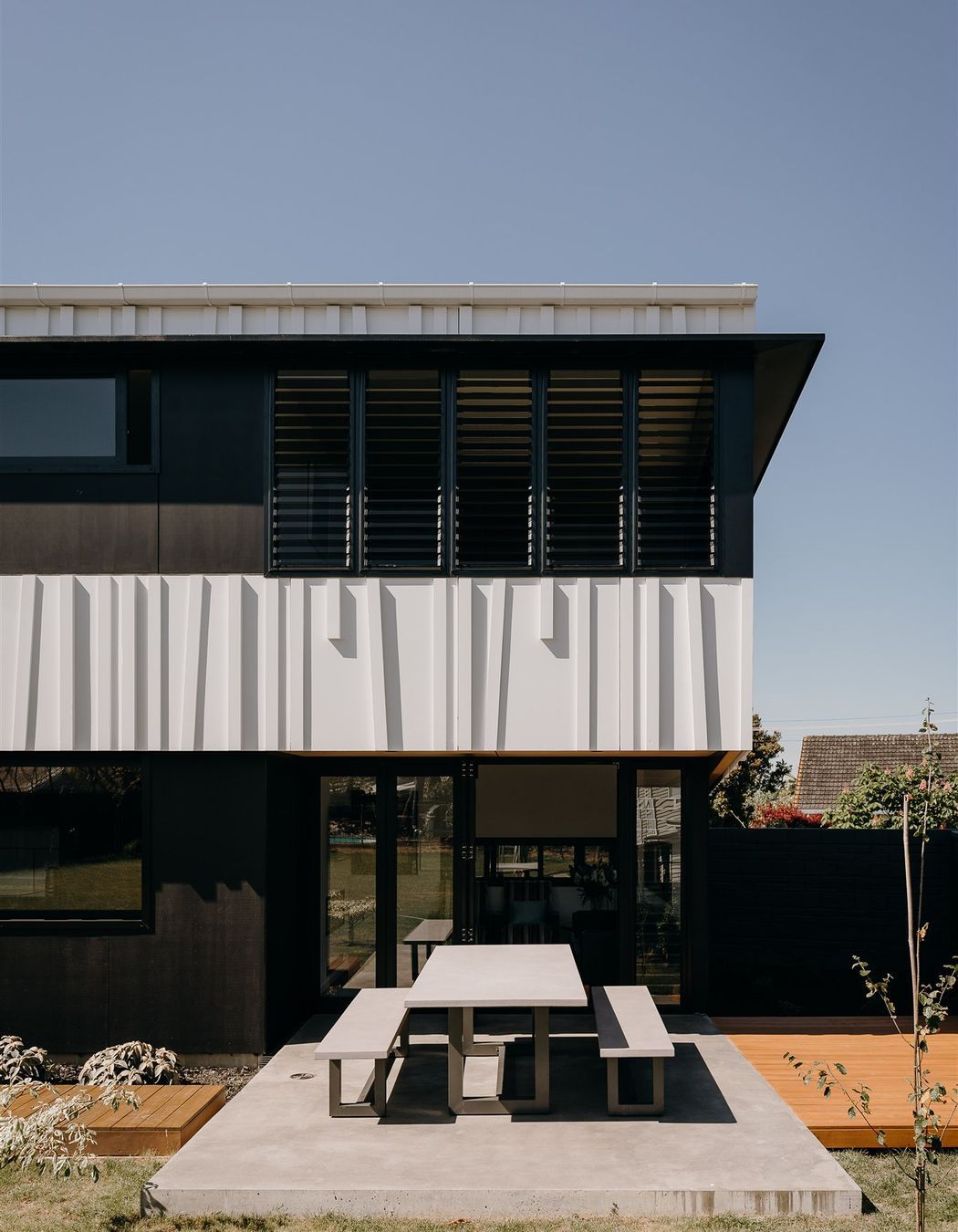 The main living area opens onto the private, rear backyard, whose central space is atop a concrete slab met on either side by timber decking that runs the length of this long, narrow house