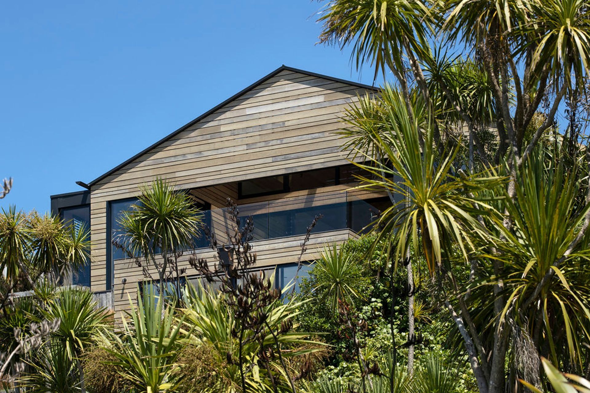 Horizontal cedar and glass define this elevation, complementing the greenery and light palette of the coastal area.