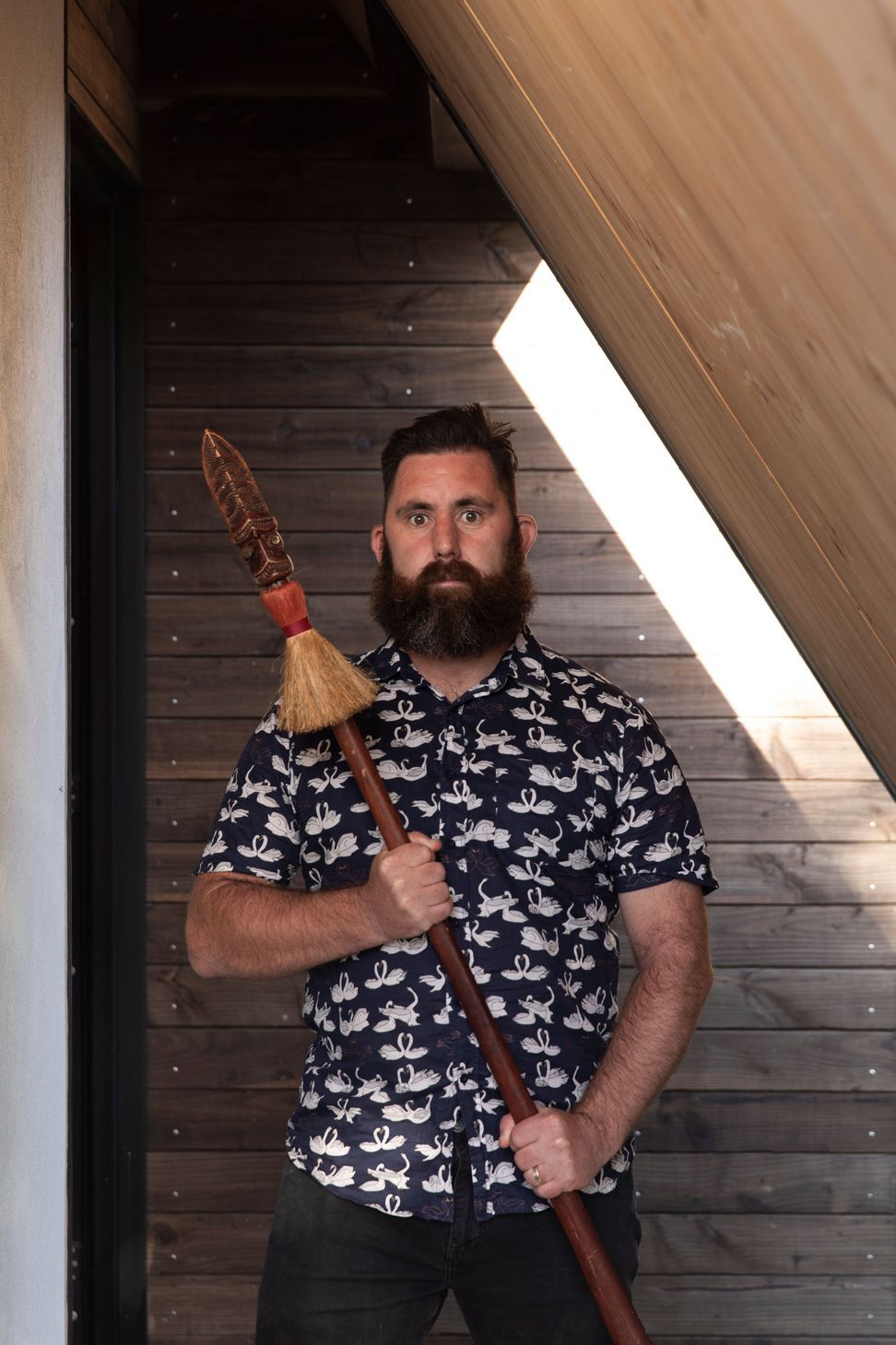 Designer Craig Wilson in the porch of his new home holding his taiaha.