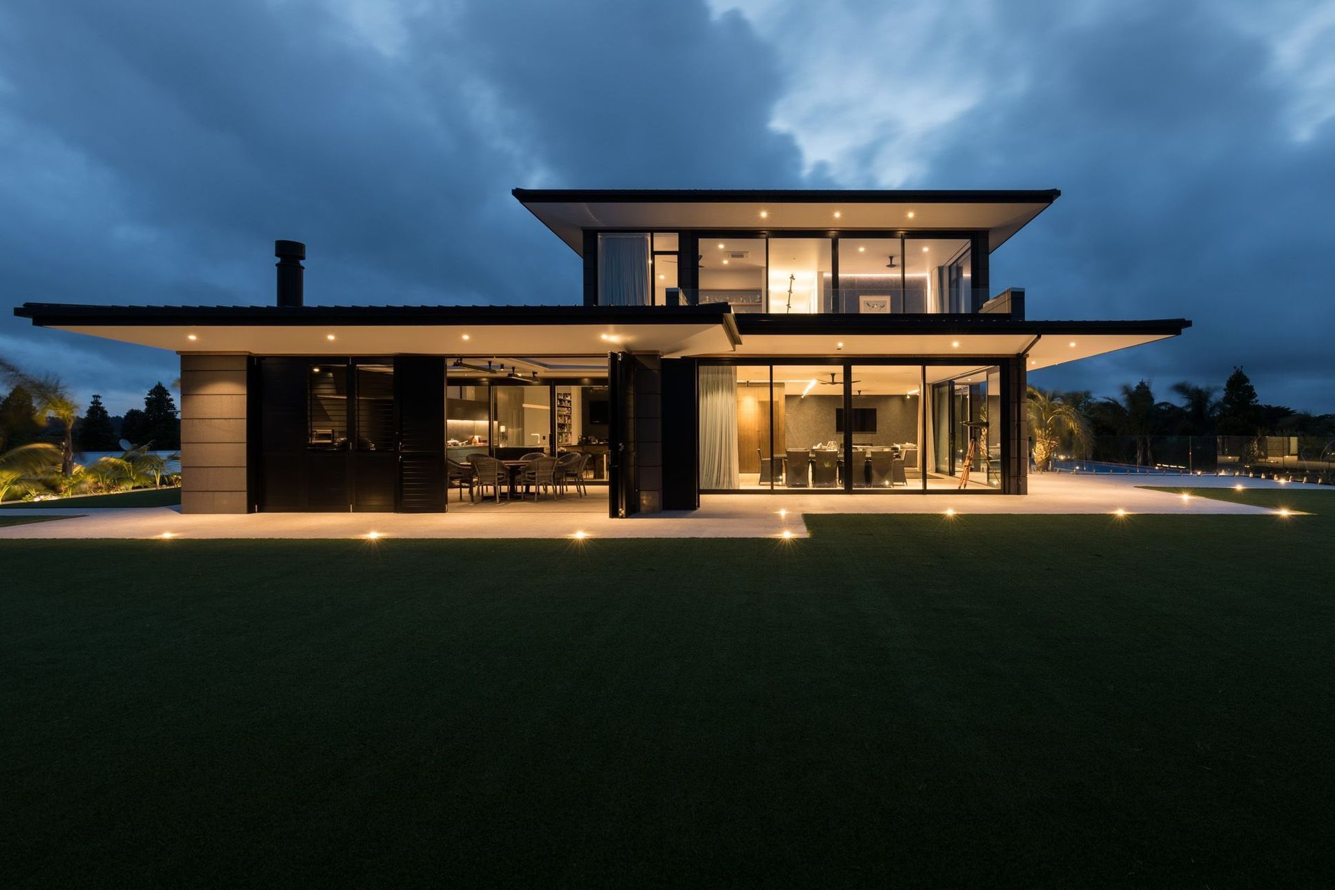 The eastern elevation lit up like a beacon at night, shows the outdoor room (left), the dining area (centre) and the swimming pool area (right).