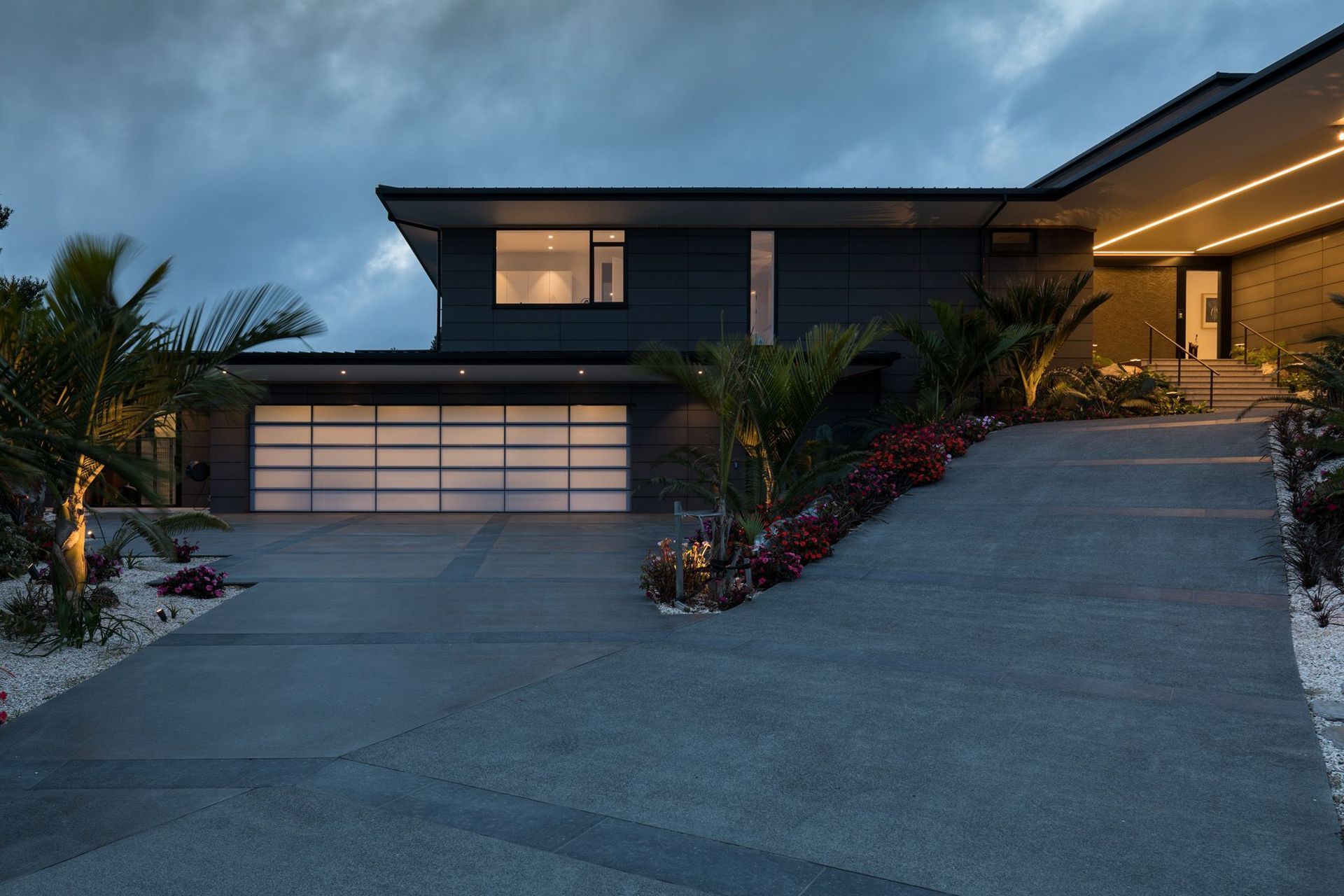 The front driveway leading the house is lined with sub-tropical plants. The garage (leftt) lights up like a lantern at night, while LED lights in the soffit direct visitors to the main entrance.