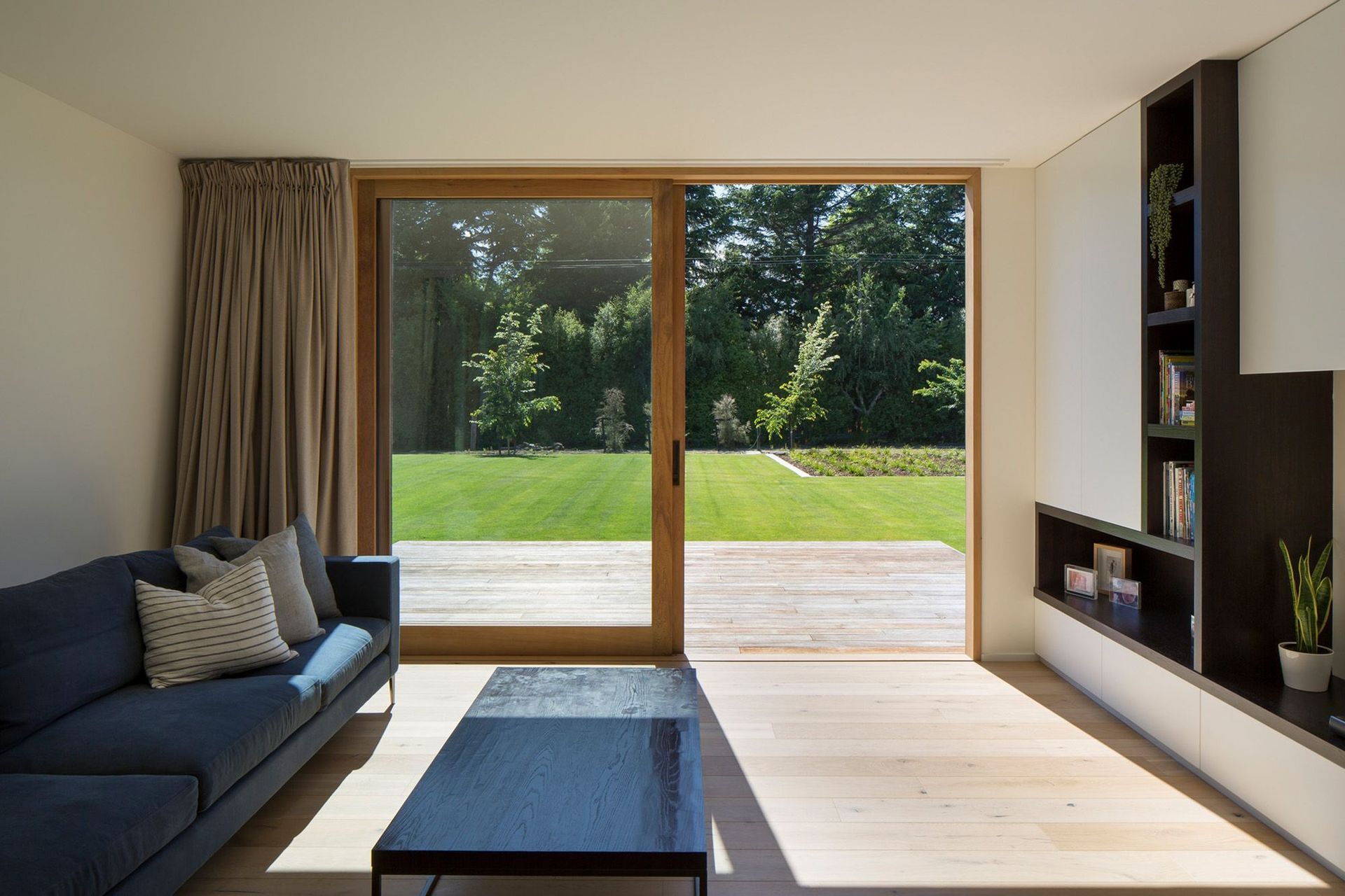 The other lounge area opens right up to a decked area and features custom-built shelving and an ink-coloured sectional sofa by Trenzseater.