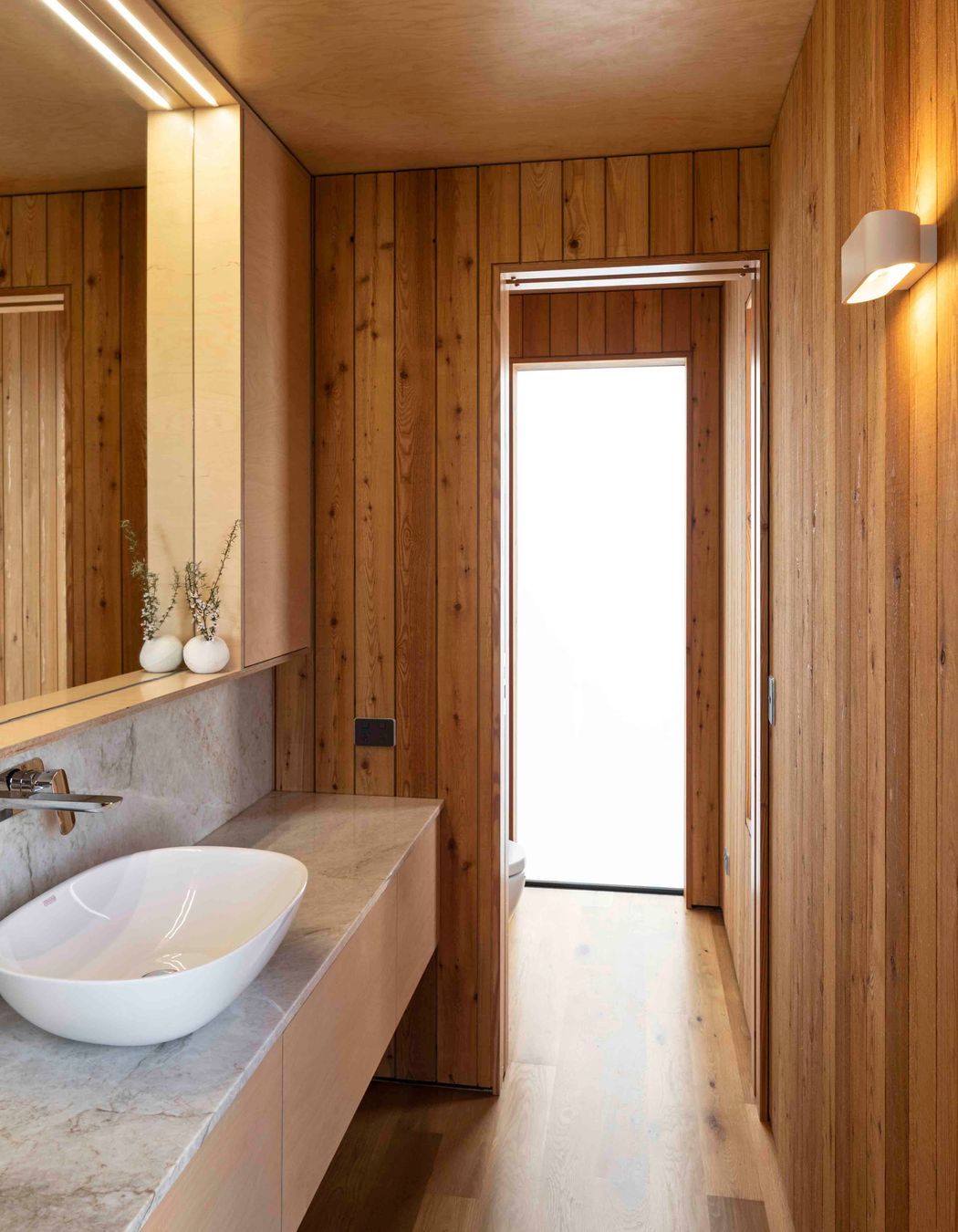 The bathroom's materiality ties easily into the biophilic theme of the house with Siberian larch walls, birch plywood ceilings and stone countertop.