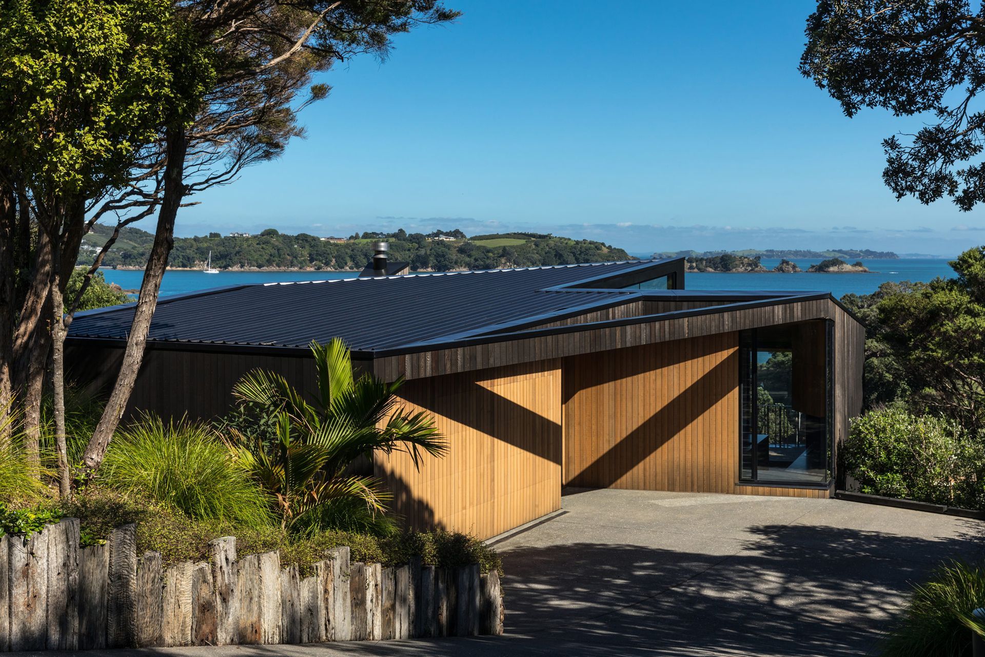 On a steep site overlooking the Hauraki Gulf, a chamfered and shadowy form settles into the landscape.