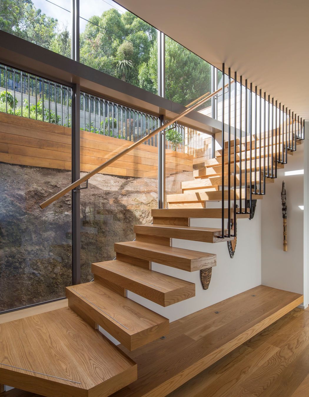Double-height glazing behind the main, cantilevered, staircase shows how the house is sitting shy of the rockface behind.
