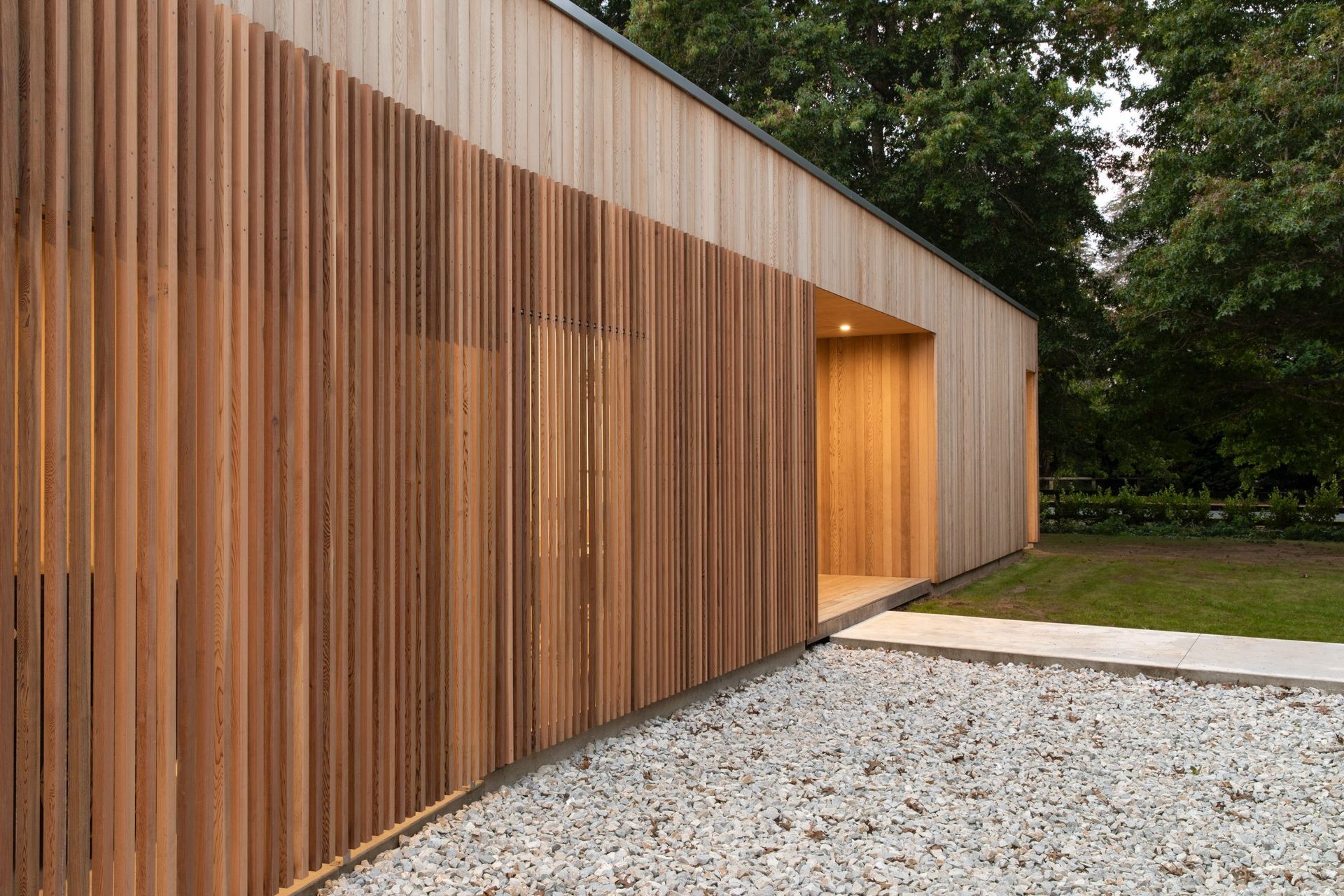 The main entrance is inset into the cedar-clad pavilion. A dramatic cedar rainscreen shields the carport from the road and filters light through the large office window.